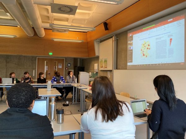 Zu sehen sind Studierende in einem Seminarraum, die einer projizierten PowerPoint folgen.